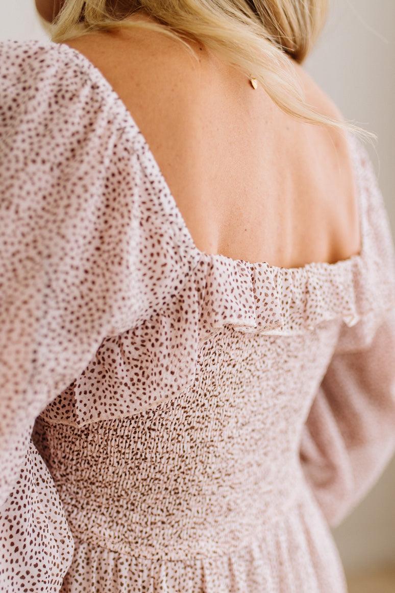 Close-up back view of a woman wearing a blush pink off-the-shoulder dress with a delicate black floral print and smocked bodice.