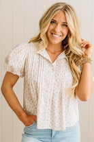 Woman wearing a white floral blouse and light blue jeans against a plain background