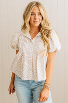 Woman wearing a white patterned blouse and light blue jeans against a neutral background