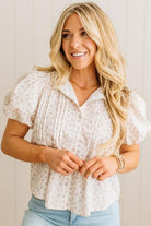 Woman wearing a white floral blouse with short sleeves against a light background