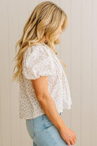 Woman wearing a white floral blouse and light blue jeans against a beige wall.