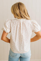 Woman wearing a white floral blouse and light blue jeans against a beige wall.