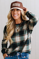 BLONDE WOMAN IN A BROWN HAT WEARING A GREEN CREW NECK, LONG SLEEVE, PLAID PRINTED HACCI TOP