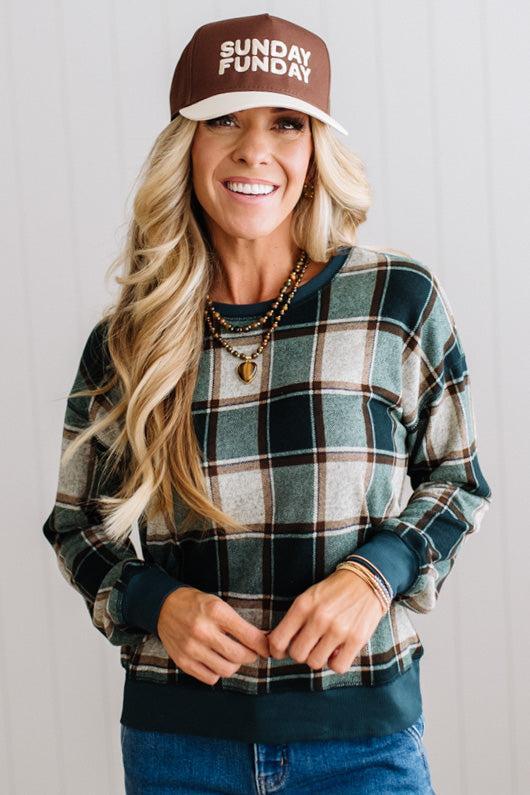 BLONDE WOMAN IN A BROWN HAT WEARING A GREEN CREW NECK, LONG SLEEVE, PLAID PRINTED HACCI TOP