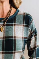 BLONDE WOMAN IN A BROWN HAT WEARING A GREEN CREW NECK, LONG SLEEVE, PLAID PRINTED HACCI TOP