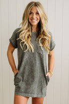 Woman wearing a gray t-shirt dress against a white wall