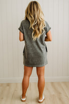 Person wearing a gray dress standing against a white paneled wall.