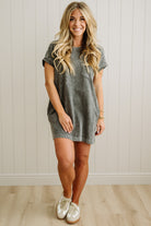 Woman wearing a gray dress standing against a white paneled wall.