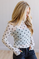 Woman wearing a white long-sleeve top with black polka dots and dark jeans.