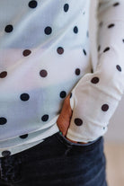Close-up of a person wearing a white shirt with black polka dots and dark pants.