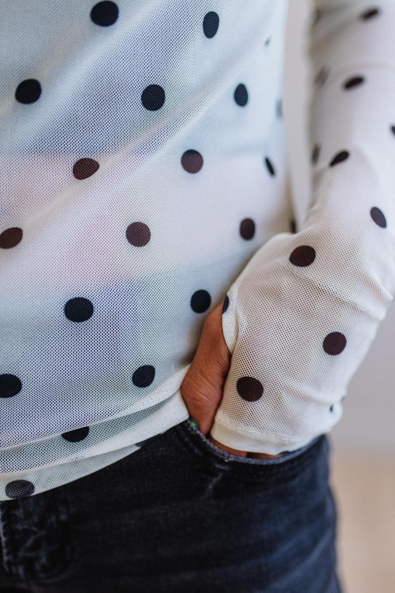 Close-up of a person wearing a white shirt with black polka dots and dark pants.