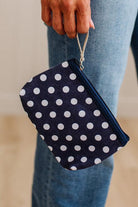 A navy blue fabric pouch with white polka dots and a silver zipper, held by a person wearing blue jeans.