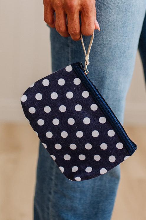 A navy blue fabric pouch with white polka dots and a silver zipper, held by a person wearing blue jeans.