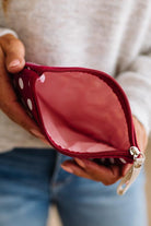 A close-up of a person holding an open red zip pouch with white polka dots. The pouch is shown from the inside, revealing a pink interior lining, with the person's hands and a light gray sweater visible in the background.