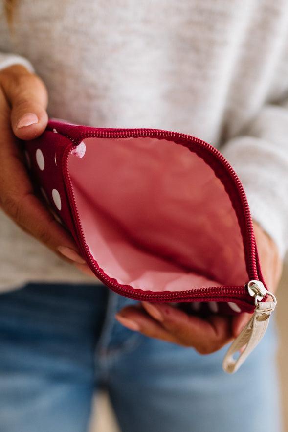 A close-up of a person holding an open red zip pouch with white polka dots. The pouch is shown from the inside, revealing a pink interior lining, with the person's hands and a light gray sweater visible in the background.