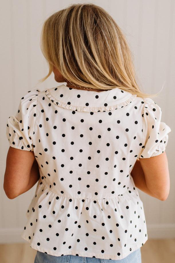 Blonde woman wearing a ivory and black Polka Dot Woven Peter Pan Collar Top with double tie front.