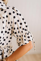 Close-up of a woman wearing a cream-colored blouse with black polka dots, featuring puff sleeves with drawstring ruffles.