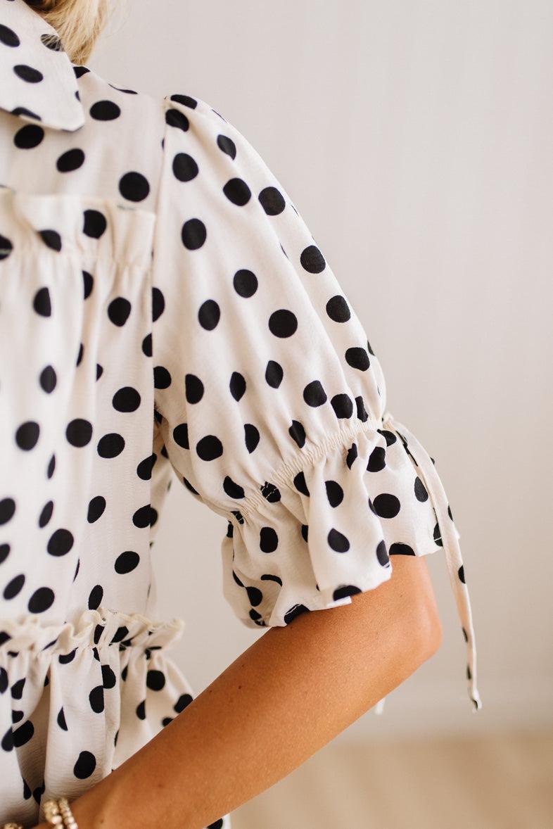 Close-up of a woman wearing a cream-colored blouse with black polka dots, featuring puff sleeves with drawstring ruffles.