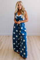 Woman wearing a blue denim jumpsuit with white polka dots against a white wall.