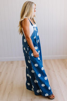 Woman wearing blue polka dot overalls standing on a wooden floor.