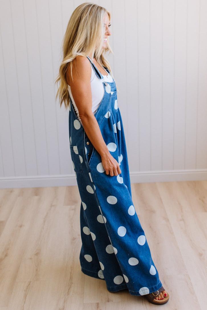Woman wearing blue polka dot overalls standing on a wooden floor.