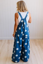 Woman wearing blue polka dot overalls against a white wall.