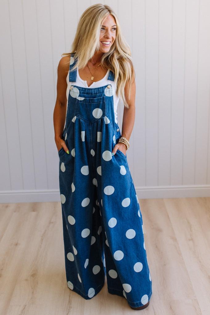 Woman wearing blue polka dot overalls against a white wall.