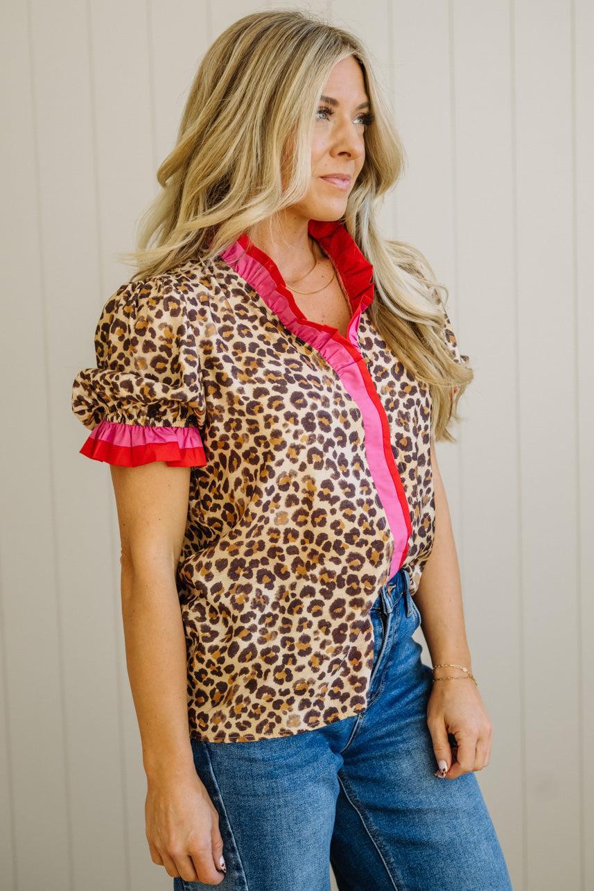 Woman wearing a leopard print blouse with pink trim and blue jeans against a neutral background