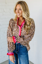 Woman wearing a leopard print top with pink accents and blue jeans against a white brick wall.