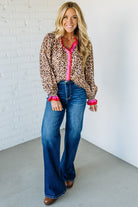 Woman wearing a leopard print shirt with pink trim and blue jeans against a white brick wall.
