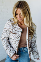 Woman wearing a patterned jacket, brown top, and blue jeans against a white background