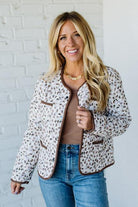 Woman wearing a patterned jacket and blue jeans against a white brick wall.