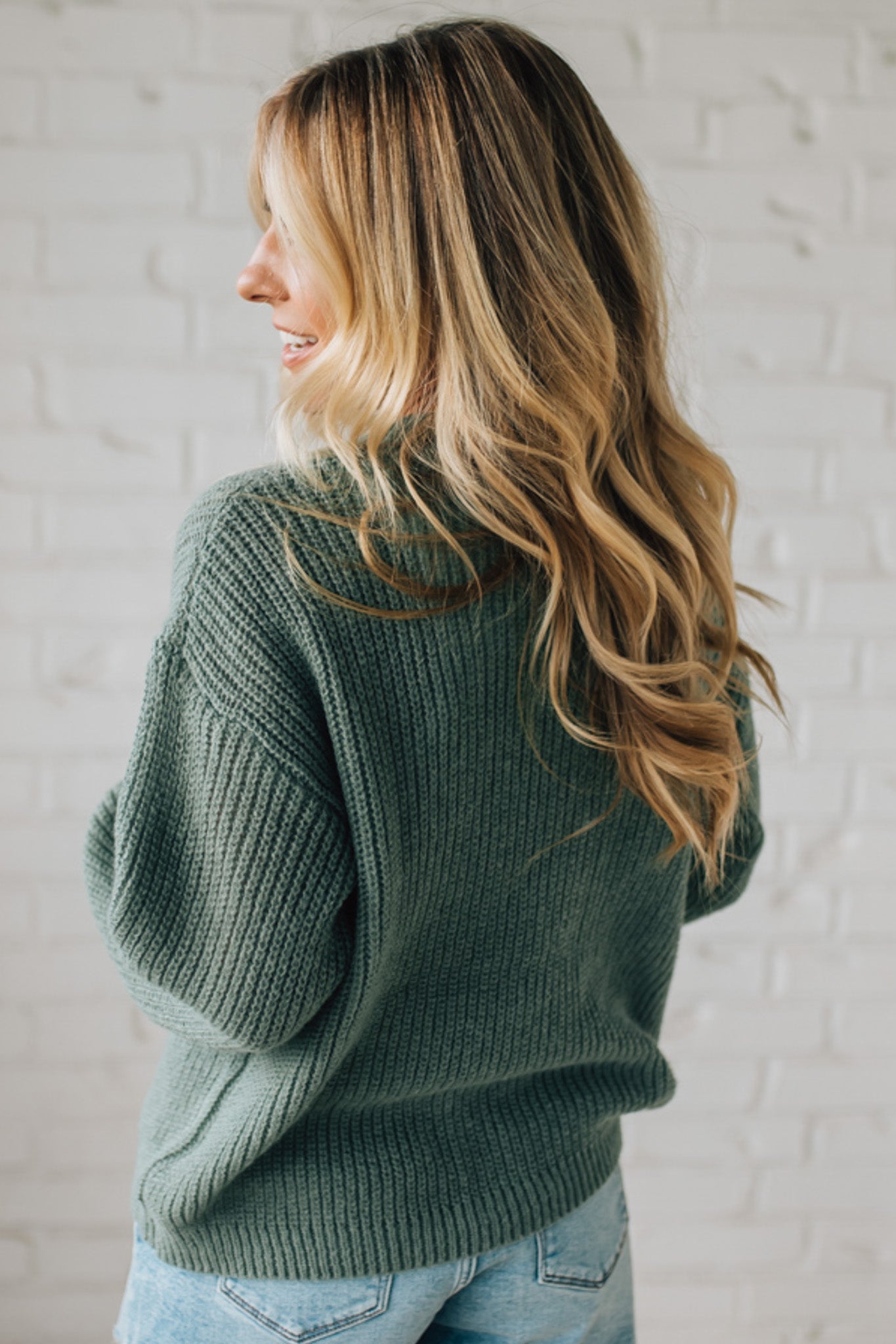 Woman wearing a green sweater against a white brick wall