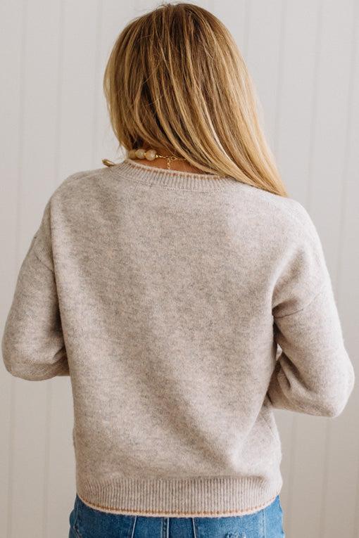 BLONDE WOMAN IN DARK JEANS WEARING A HORSE JACQUARD, STITCH TRIM ACCENT, LONG SLEEVE, CREW NECK PULLOVER SWEATER WITH A HORSE ON THE FRONT, AND WEARING A BIG BELT BUCKLE TOO.
