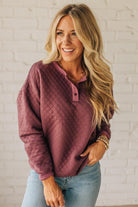 Woman wearing a quilted purple pullover with a white brick wall background