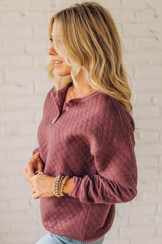 Woman wearing a maroon quilted sweater against a white brick wall