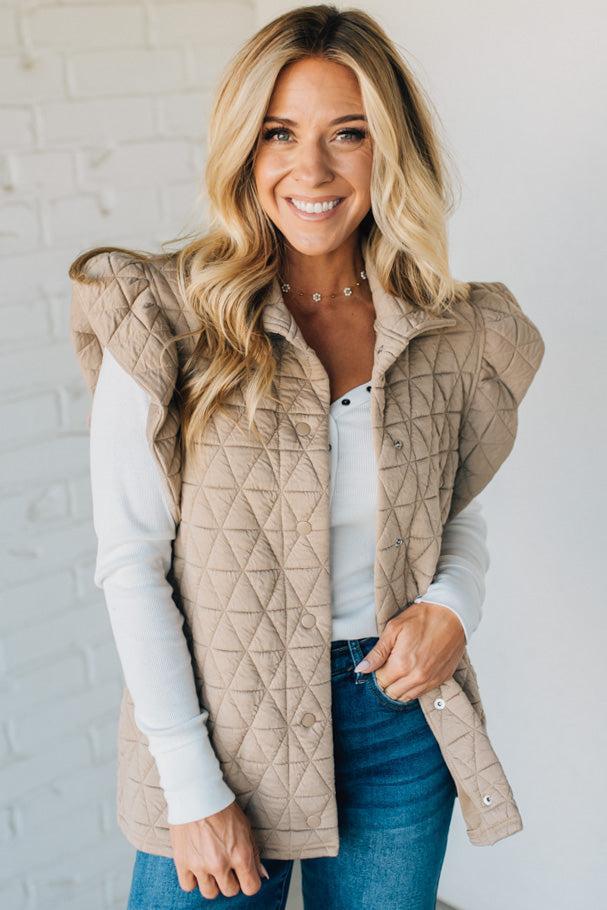 Woman wearing a beige quilted vest against a white brick wall
