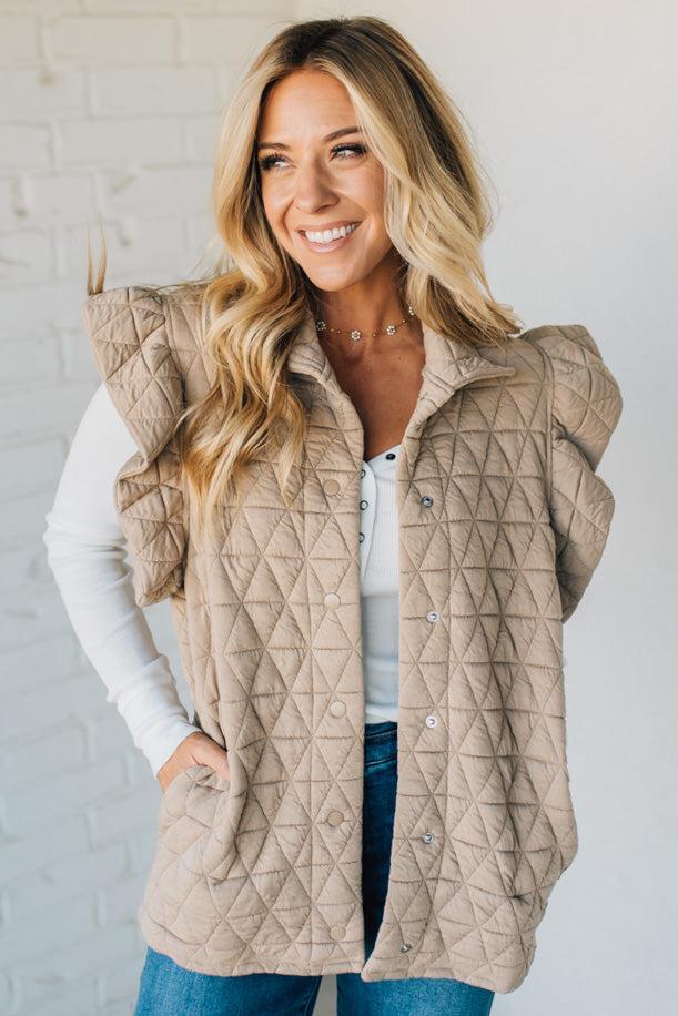 Woman wearing a beige quilted vest against a white brick wall