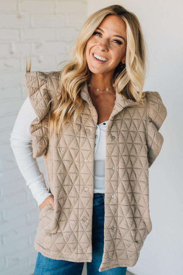 Woman wearing a beige quilted vest against a white brick wall