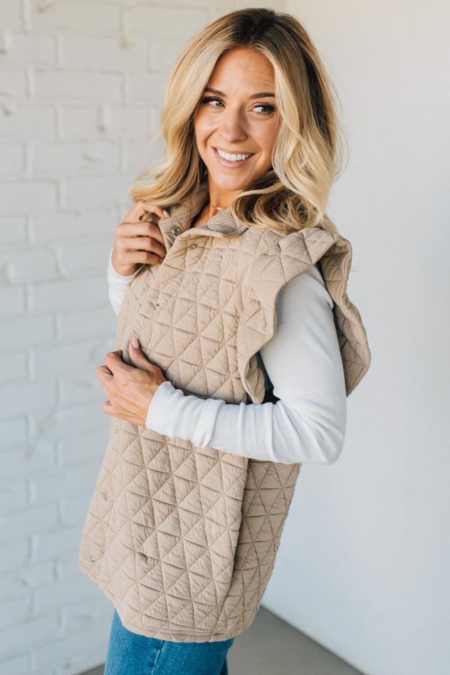 Woman wearing a beige quilted vest against a white brick wall