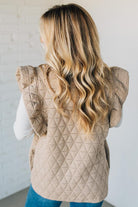 Person wearing a beige quilted vest against a white background