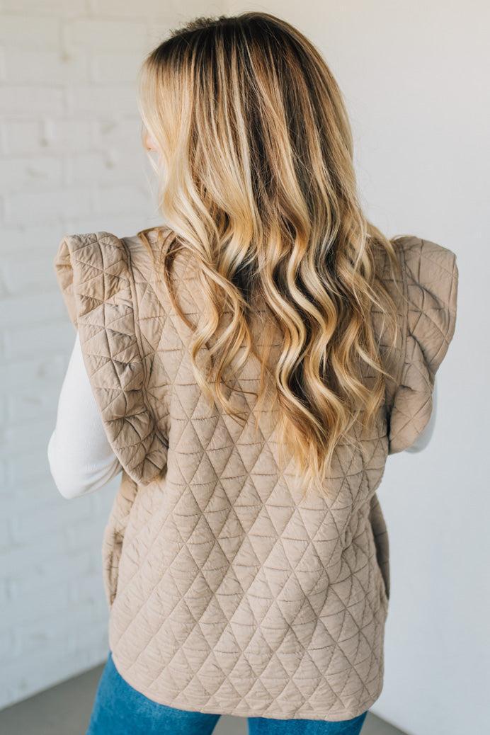 Person wearing a beige quilted vest against a white background