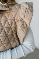 Quilted beige blanket draped over a chair with a neutral background