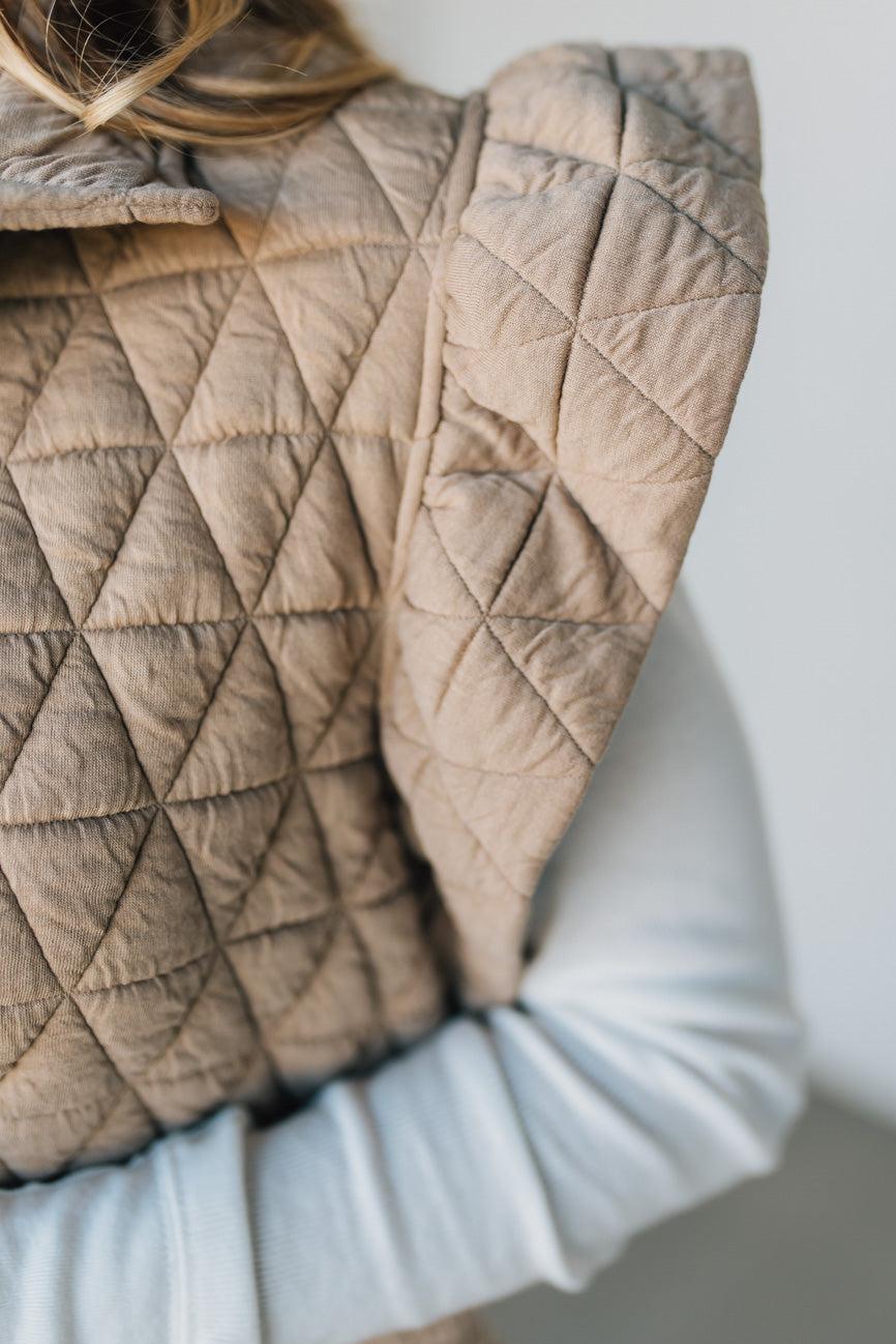 Quilted beige blanket draped over a chair with a neutral background
