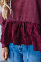 Close-up of a burgundy top with lace details and blue jeans.