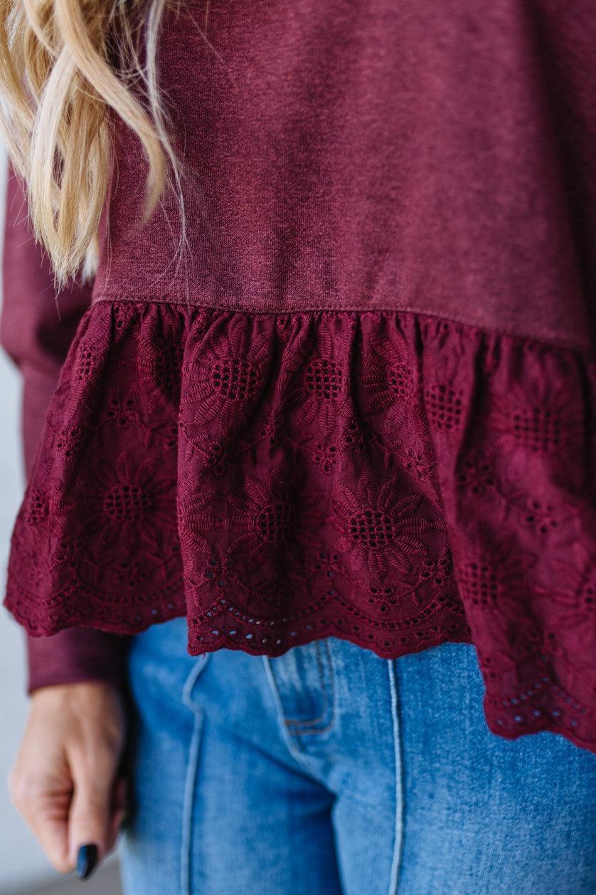 Close-up of a burgundy top with lace details and blue jeans.