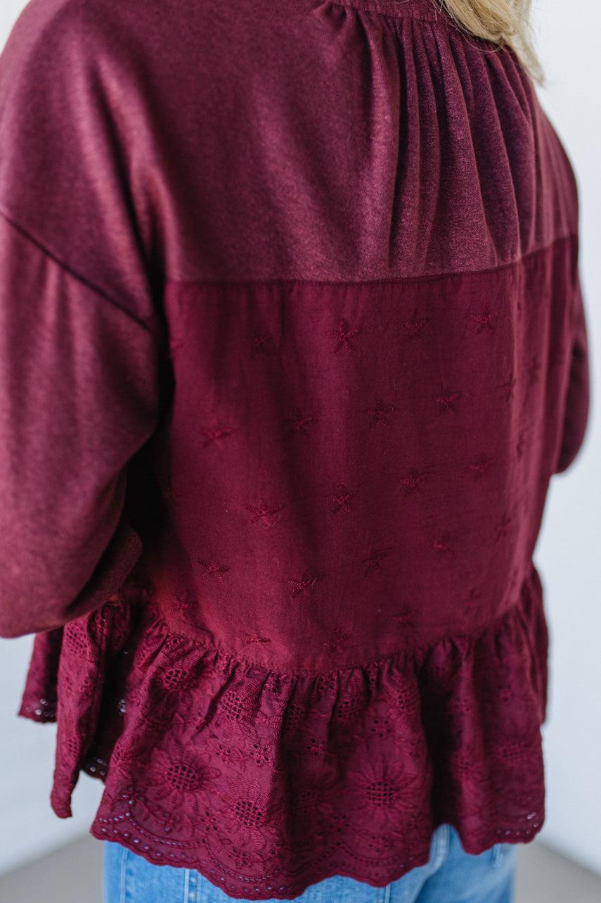 Maroon blouse with lace details and blue jeans on a white background