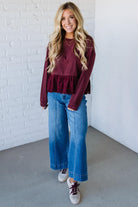 Woman wearing a burgundy ruffled top and blue jeans against a white brick wall.