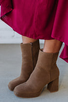 Person wearing brown ankle boots with block heel and smooth faux suede finish.