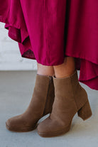 Person wearing brown ankle boots with block heel and smooth faux suede finish.